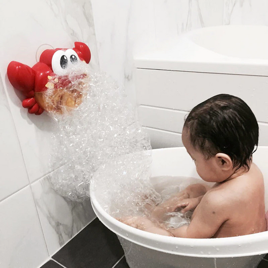 Child in a bathtub with bubbles and a red crab-shaped toy on a tiled bathroom wall.